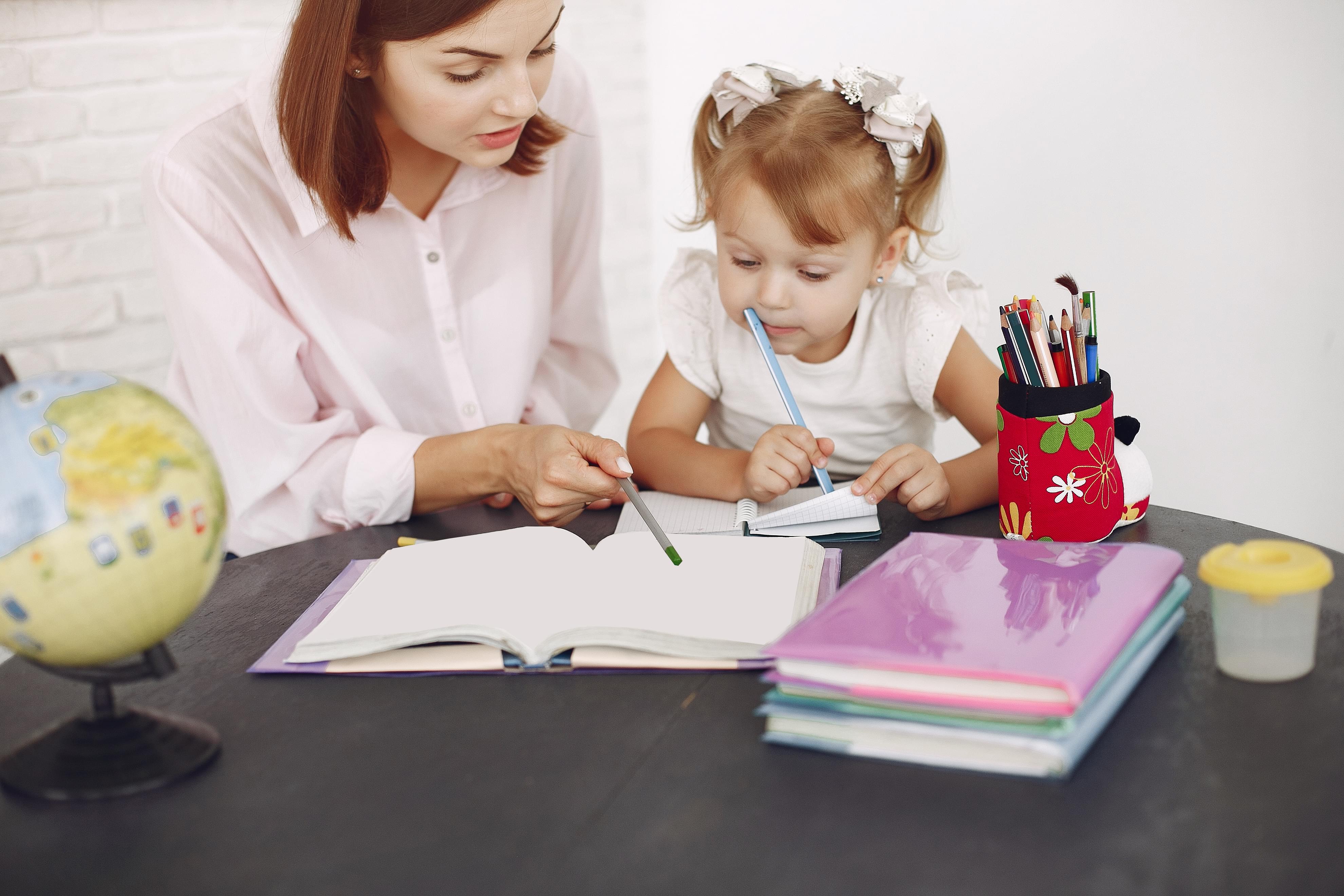 pre kindergarten child and tutor looking and pointing at notebook